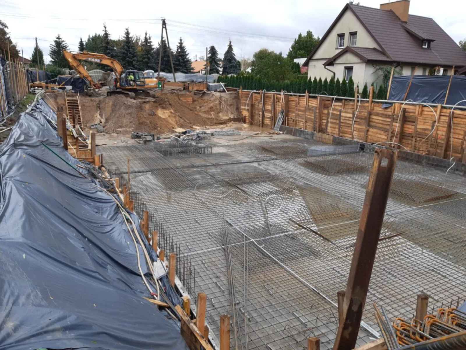 Wykop pod fundament z szalunkiem i zbrojeniem, koparka w tle